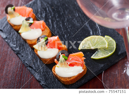 Delicious sandwiches with salmon, green onions, olives and white sauce on a cutting board Delicious sandwiches with salmon, green onions, olives and white sauce on a cutting board 75547151