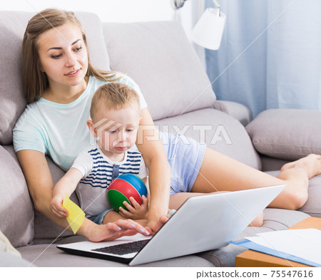 Satisfied mother with child is productively working behind laptop 75547616