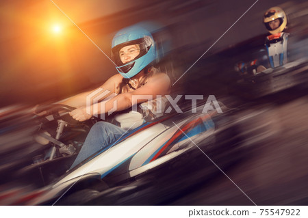 Girl and her friends competing on racing cars at kart circuit Girl and her friends competing on racing cars at kart circuit 75547922