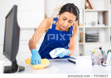 Focused Hispanic workwoman in overalls cleaning office 75548037