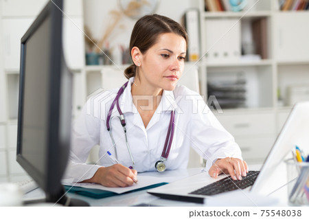 Female physician filling up medical forms on laptop 75548038