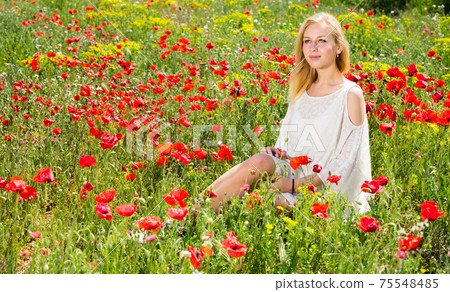 Beautiful woman wearing white dress sitting in poppy field and enjoying Beautiful woman wearing white dress sitting in poppy field and enjoying 75548485