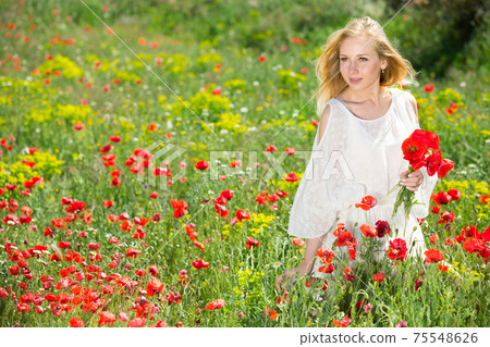 Beautiful young female in white dress holding bouquet of poppy flowers 75548626