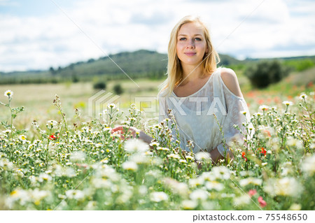 Young girl in white dress sitting in field of wild chamomile flowers Young girl in white dress sitting in field of wild chamomile flowers 75548650