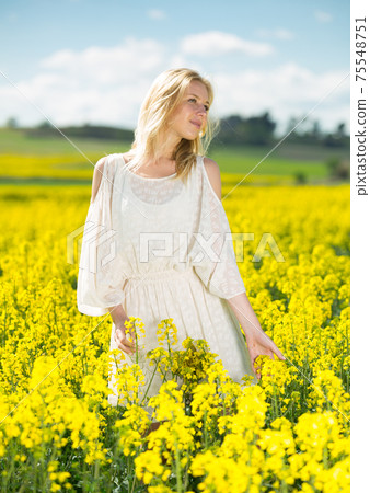Young woman in yellow oilseed rape field posing in white dress Young woman in yellow oilseed rape field posing in white dress 75548751