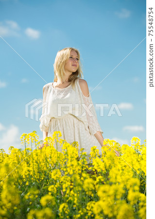 Girl posing in rape seed flowers field posing in white dress at sunny day Girl posing in rape seed flowers field posing in white dress at sunny day 75548754