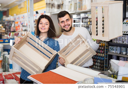 Young smiling couple demonstrating boxes for decorating house in paint store Young smiling couple demonstrating boxes for decorating house in paint store 75548901