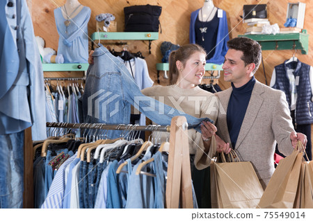 Smiling woman and man are choosing clothes and looking on jeans jacket Smiling woman and man are choosing clothes and looking on jeans jacket 75549014