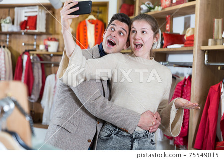 Smiling couple is satisfied of purchases and taking selfie 75549015