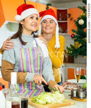 Two young women friends in xmas hats cooking christmas dinner Two young women friends in xmas hats cooking christmas dinner 75549039