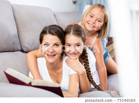 Mom reads tales for her daughters lying on sofa Mom reads tales for her daughters lying on sofa 75549165