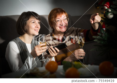 Happy mother and daughter drink champagne and watch TV on Christmas night 75549419