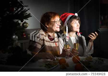 Happy mother and daughter drink champagne and watch TV on Christmas night 75549428