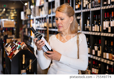 Woman choosing bottled wine in wineshop 75549774