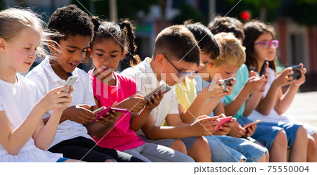 Children using mobile devices outdoors at sunny day Children using mobile devices outdoors at sunny day 75550004