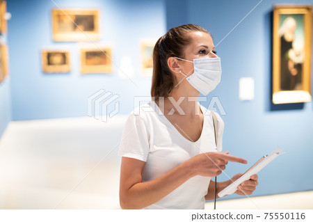 Woman in mask observing artworks in museum 75550116
