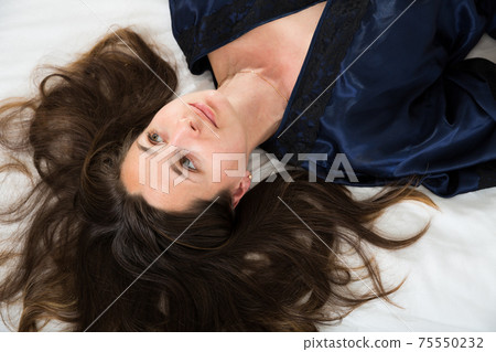 Top view of young woman in bathrobe is relaxing in bed at home Top view of young woman in bathrobe is relaxing in bed at home 75550232