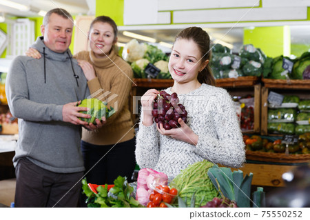 Girl holding grapes with family in fruit store Girl holding grapes with family in fruit store 75550252