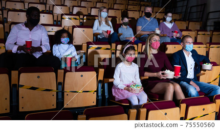 Men, women and children in protective masks sitting in cinema auditorium 75550560