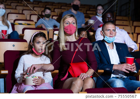 Friendly family in protective masks watching movie in cinema 75550567