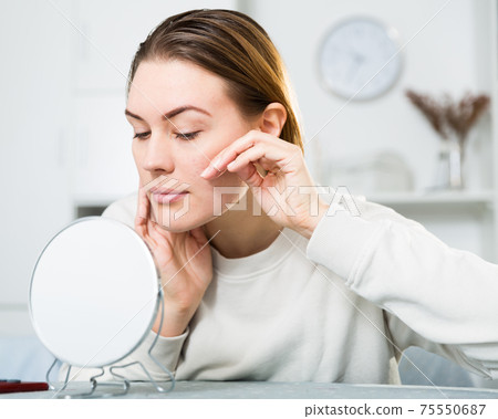 Smiling female is looking on her skin in the mirror 75550687