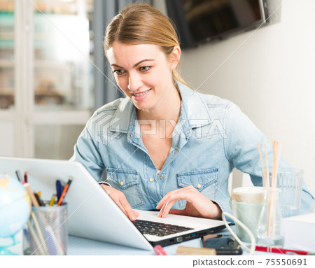 Smiling girl sitting at table at home calculating domestic finances and bills Smiling girl sitting at table at home calculating domestic finances and bills 75550691