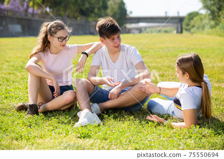 Group of teenagers chatting while sitting on green lawn Group of teenagers chatting while sitting on green lawn 75550694