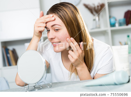Smiling female is looking on her skin in the mirror Smiling female is looking on her skin in the mirror 75550696