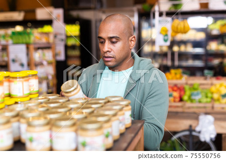 Man reading jar contents on label while shopping in supermarket Man reading jar contents on label while shopping in supermarket 75550756