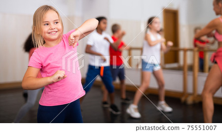 Preteen girl practicing dance movements with group of children Preteen girl practicing dance movements with group of children 75551007