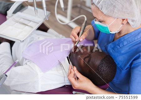 Dentist is treating male patient which is sitting in dental chair 75551599