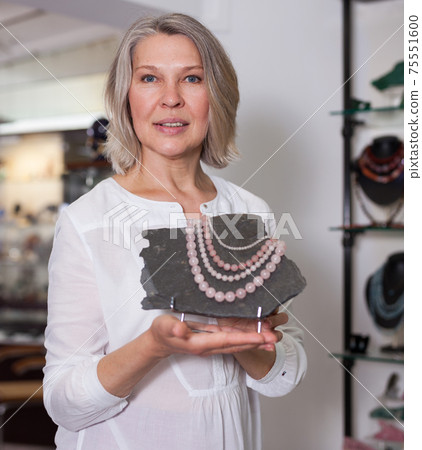Woman offering to buy fashionable rose quartz necklace in the shop of jewelry Woman offering to buy fashionable rose quartz necklace in the shop of jewelry 75551600