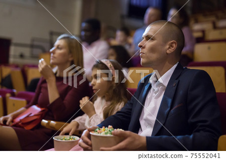 Interested man absorbedly watching movie in picture theater Interested man absorbedly watching movie in picture theater 75552041