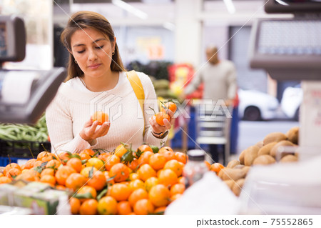 Female shopper selects ripe tangerines in grocery hypermarket Female shopper selects ripe tangerines in grocery hypermarket 75552865