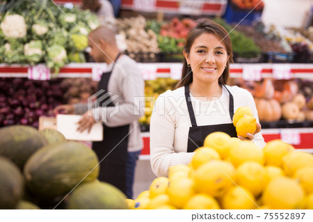 Merchandiser lays out ripe lemons on the shelves in supermarket Merchandiser lays out ripe lemons on the shelves in supermarket 75552897