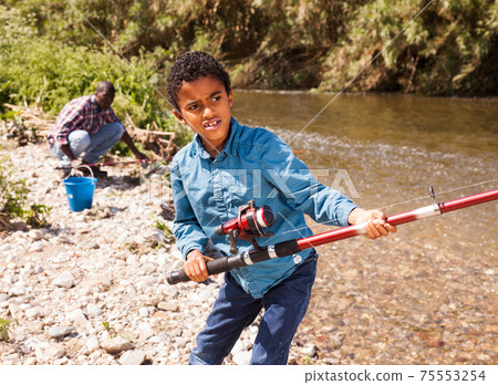 Boy pulling fish from river Boy pulling fish from river 75553254