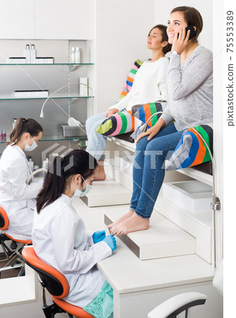 Woman relaxing in nail salon on pedicure and using phone Woman relaxing in nail salon on pedicure and using phone 75553389