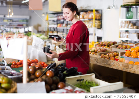 Positive girl buying aubergines at market 75553407