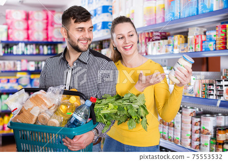 Portrait of couple with shopping basket filled food products Portrait of couple with shopping basket filled food products 75553532