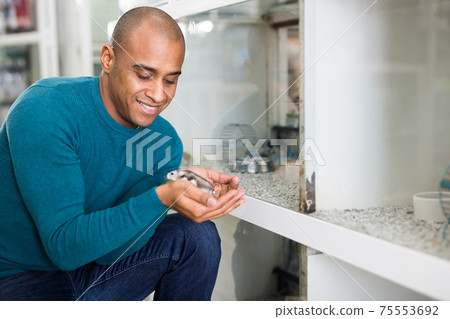 Man shopping in pet shop holding hamster Man shopping in pet shop holding hamster 75553692