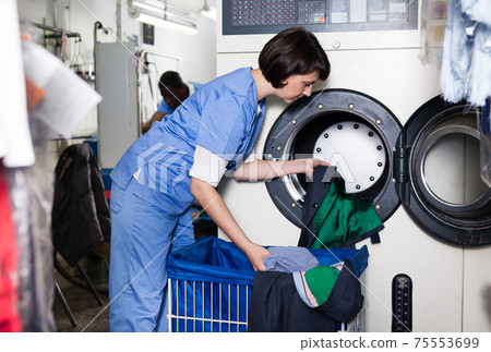 Female worker loading laundry washing machine Female worker loading laundry washing machine 75553699