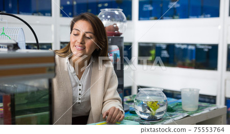 Portrait of interested young woman looking at colorful tropical fish in aquariums in shop Portrait of interested young woman looking at colorful tropical fish in aquariums in shop 75553764