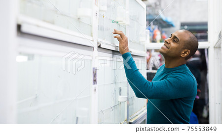 Portrait of interested man looking at tropical parrot in cage Portrait of interested man looking at tropical parrot in cage 75553849