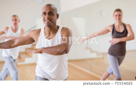 Cheerful Latino practicing vigorous dance in group class Cheerful Latino practicing vigorous dance in group class 75554085