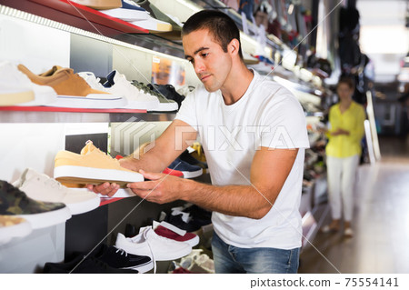 Positive male customer choosing sneakers Positive male customer choosing sneakers 75554141