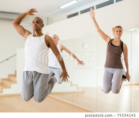 Hispanic man jumping during group choreography in dance studio 75554143