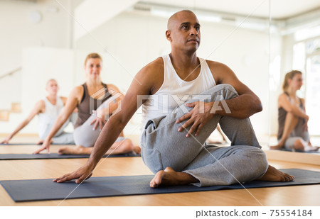Latin american man practicing Matsyendrasana during group yoga training Latin american man practicing Matsyendrasana during group yoga training 75554184