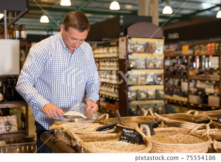 Male customer choosing nuts in average food shop Male customer choosing nuts in average food shop 75554186