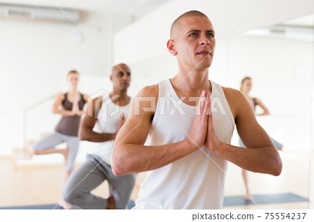 Man standing in Eka Pada Pranamasana during group yoga training Man standing in Eka Pada Pranamasana during group yoga training 75554237