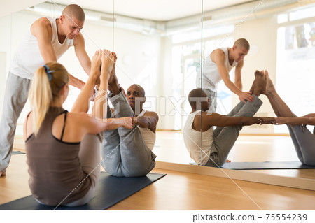Woman and man performing paired yoga exercises with instructor 75554239